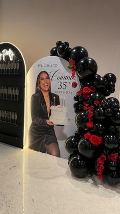 a woman holding a birthday cake in front of a sign with roses and candles on it