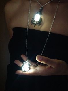 a woman holding two glowing necklaces in her hand with the light shining through them