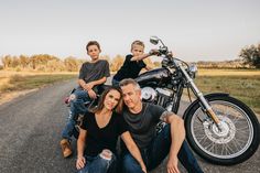 a man, woman and two boys sitting on a motorcycle in the middle of an empty road