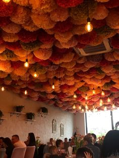 people sitting at tables in a restaurant with paper flowers hanging from the ceiling above them