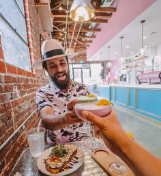 a man in a fedora is holding a bowl of food at a table with other people