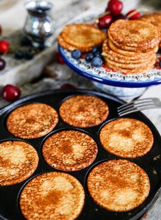 some pancakes and blueberries are in a pan on a table next to silverware