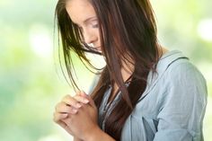 a woman with long hair holding her hands together and looking down at the ground while she is praying