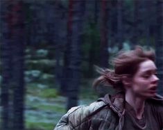 a woman is walking through the woods with her hair blowing in the wind