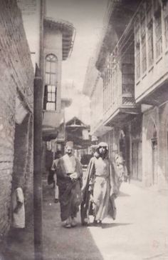 an old black and white photo of two men walking down the street in front of some buildings