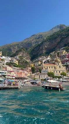 boats are docked in the water next to buildings on a hill side with mountains in the background