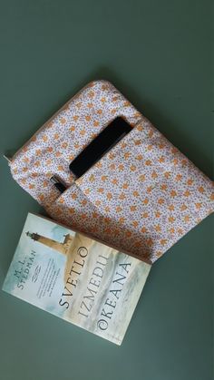 an orange and white flowered bag next to a book on a green table top