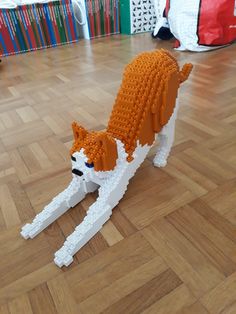 an orange and white dog made out of legos sitting on the floor next to bookshelves