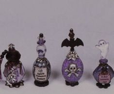 five miniature bottles are lined up in a row on a white surface, one is decorated with skulls and the other has a bat