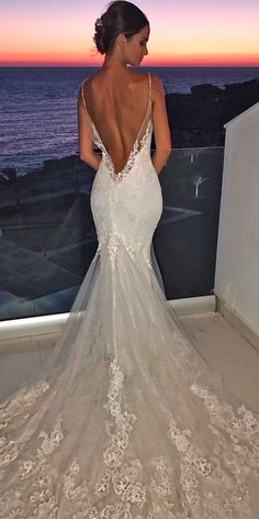 a woman in a wedding dress looking out at the ocean with her back to the camera