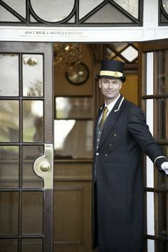 a man in a suit and hat standing at the entrance to a building with an open door