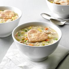 two white bowls filled with chicken pot pie soup on top of a table next to silverware