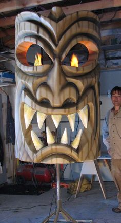 a man standing next to a large wooden mask