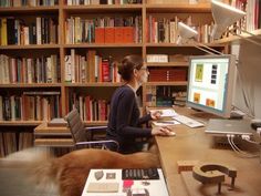 a woman sitting at a desk in front of a computer monitor with bookshelves behind her