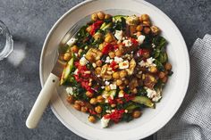 a white bowl filled with vegetables and chickpeas next to a glass of water