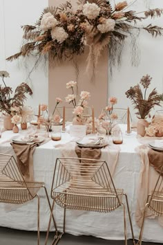 the table is set with pink and white flowers, gold chairs, and greenery