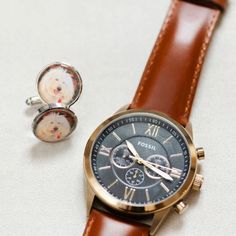 a watch and cufflinks sitting next to each other on a white table top