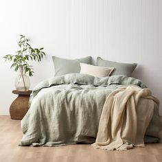 a bed with green sheets and pillows in a white room next to a potted plant