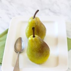 two green pears on a white plate with a spoon