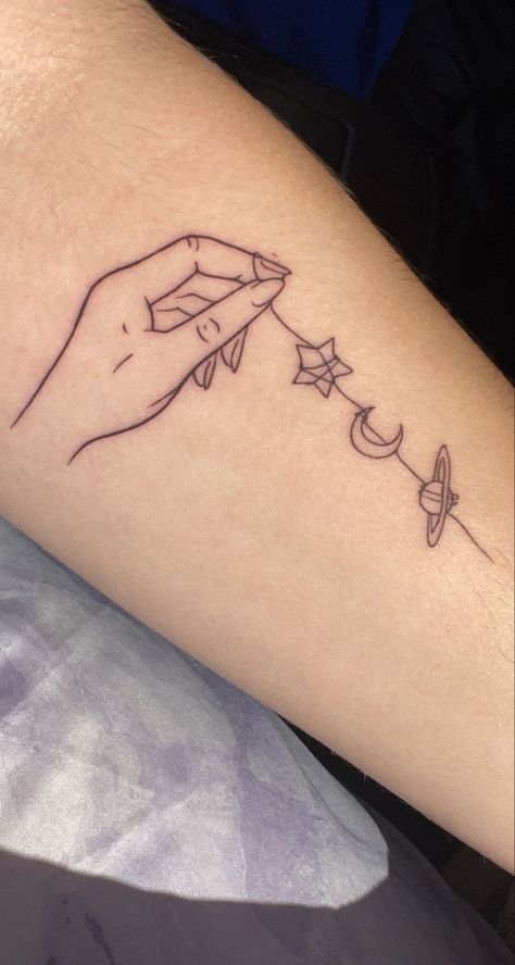 fine line tattoo of a hand holding a string with a star, the moon, and a planet on it. Hanging The Moon Tattoo, Moon And Earth Tattoo, Sun Moon And Planet Tattoo, Hands Holding Planets Tattoo, Hand Holding Planets Tattoo, Sibling Star Tattoo, Holding Moon Tattoo, All Of The Stars Have A Reason Tattoo, Siblings Line Art