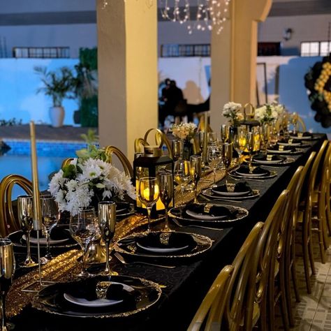 Elevate your party table arrangement with the sophistication of a black tablecloth paired with a standout sequin gold runner. Create a charming ambiance by arranging candles in holders and showcasing white florals in vases for added allure. To complete this transformation, add a touch of class with black chargers, black napkins, gold cutlery, and clear glasses. Black And Gold Dinner Party Table Decor, Black And Gold Table Centerpieces, Gold Party Decorations Diy, Black And Gold Table Setting, Gold Table Centerpieces, Black And Gold Centerpieces, Gold Table Decorations, Elegant Table Decorations, Black And Gold Party Decorations