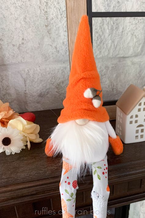 Vertical image of a gnome with a white beard, orange hat, felted acorns, and long legs sitting on a mantle with fall florals and mini ceramic houses. Diy Gnome Doll, No Sew Gnome, Swedish Gnomes, Gnome Sewing Pattern, Gnome Sewing, Gnome Beard, Gnome Shelf Sitter, Boot Pattern, Gnome Ideas