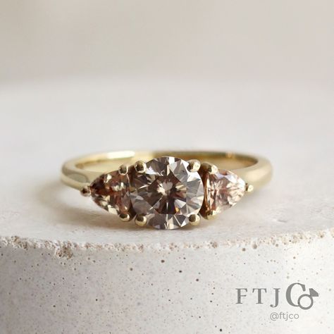 This beautiful bronze-coloured diamond three stone ring won't stick around for long, but it *is* currently available in our Ready to Wear collection..! The tone-on-tone layering of the bronze-y brown diamond, champagne side stones, and yellow gold is super modern and elegant. Come try it on in the store, but don't wait too long, it's gonna go fast! 😍💍💨 . This is our Emilia Three Stone Ring, made in 18K AKARA People+Planet yellow gold. It features a 0.97 ct Round Brilliant Cut Antique Bronze L Rough Diamond Ring, Brown Diamond, Three Stone Rings, Rough Diamond, Wedding Dress Ideas, Rings Bracelets, Ready Made, Three Stone, Round Brilliant Cut