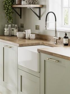 Pale enough to work as a neutral, the sage green tone of these sturdy, 20mm-thick doors makes a great choice for those that want a subtle style with plenty of country character. Choose from a wide variety of cupboards, such as larder units, which can keep cooling devices hidden from view to help maintain an uninterrupted design. Kitchen Pale Green, Howdens Elmbridge Sage Green, Country Kitchen Colour Schemes, Light Kitchen Cupboards, Heritage Sage Kitchen, Small Sage Kitchen Ideas, Sage Green Vintage Kitchen, Japandi Kitchen Sage Green, Olive Green Country Kitchen