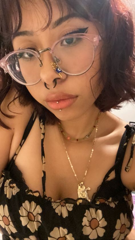 Female with short dark red hair. Wearing round purple glasses. Has a stretched 8 gauge septum with black horseshoe jewelry. Wearing an evil eye gold nose cuff. Has a vertical labret piercing with titanium jewelry. Is wearing a yellow flower and black spaghetti strap top. Has a gold necklace with a cross, and a shorter, seed beed flower necklace. Stretch Septum, Vertical Labret Piercing Jewelry, Central Labret Piercing, Vertical Labret Piercing Aesthetic, Vertical Labret Jewelry, Vertical Piercing, Central Labret, Septum Stretching, Cosmetic Aesthetic