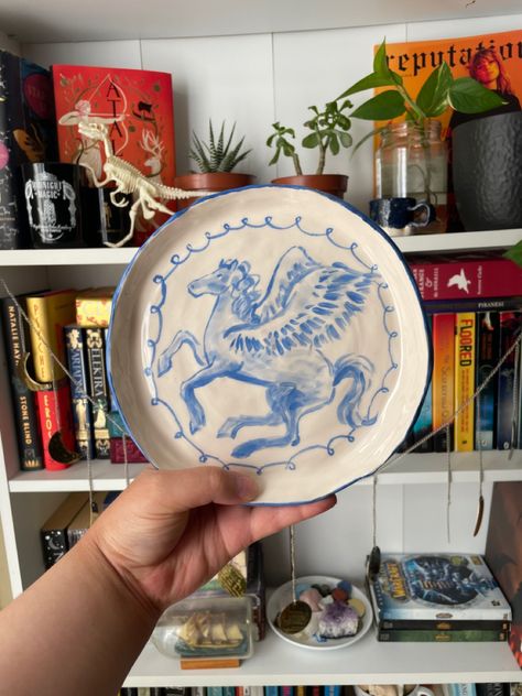 A ceramic plate with Pegasus painting decorated on it being held up against a full bookshelf in the background. Greek Mythology Pottery, Greek Mythology Decor, Dr Belongings, Watercolour Effect, Painted Illustration, Hand Built Pottery, Modern Pottery, Mythology Art, Ceramics Projects