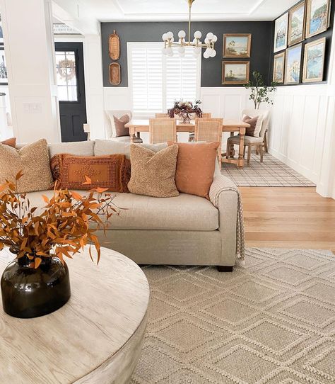 Orange throw pillows decorate a beige couch seated on a beige braided diamond pattern area rug. The couch is paired with a whitewashed wood drum coffee table in this living room next to the dining room. Pillows For Orange Couch, Couch Pillows For Tan Couch, Beige Microfiber Couch Living Rooms, Curtains To Match Tan Couch, Sandy Couch Living Room, Beige Gray Couch Living Room, Grey And Beige Couch Living Room, How To Decorate A Beige Couch, Burnt Orange Couch Pillows