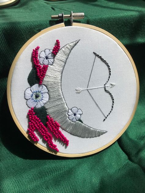 An embroidery piece of a silver moon, with red beaded flowers, and a black and silver bow and arrow, in a bamboo hoop. Goddess Embroidery, Artemis Greek Goddess, Goddess Artemis, Artemis Goddess, Goddess Of The Hunt, Apollo And Artemis, Goddess Of The Moon, Dmc Embroidery, Bow And Arrow