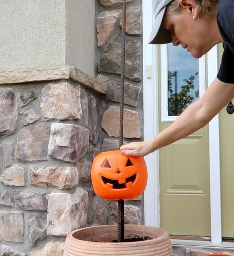 What says fall more than pumpkins? Here is a super easy and inexpensive way to dress up your porch for fall.    Step 1: Get pumpkins  Run, do not walk, to Walmart where plastic pumpkin pails are only $1.00 while supplies last. For one planter, purchase 5 pumpkins.    Step 2: Rebar  Purchase 4' rebar rods and place them into a pot (yellow circles). Secure with stones and soil. I made two planters so I purchased 2 rebar rods and 10 pumpkins.    Step 3: Cut the Handles  We don't need the… Fall Porch Pots With Pumpkins, Stacked Pumpkins In Planter, Pumpkin In Flower Pot, Fence Post Pumpkins Diy, Plastic Pumpkin Tower Diy, Walmart Pumpkin Crafts, Pumpkin Porch Decorations Diy, Pumpkin Outside Decor, Pumpkin Bucket Planter