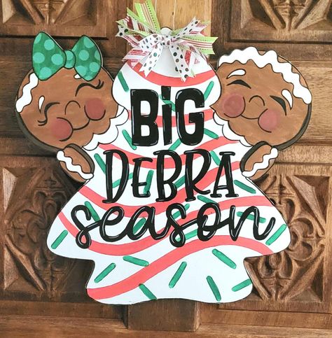 Transform your front door with our whimsical Big Deborah Season wooden door sign. This is hand-painted with a delightful Gingerbread Man design and topped with holiday ribbon that will bring joy and laughter to your festive decor. Perfect for spreading holiday cheer or as a funny gift for friends and family, this large sign is not just a decoration; it's a conversation starter that will make your entrance unforgettable!       - Hand-painted and comes with a wire hanger and ribbon bow on top. Ribbon may be different than shown in picture depending on availability.       - Sprayed with a sealer to make it suitable for outdoor use, but it is highly recommended to hang this  sign out of the direct elements. We are not responsible for any damage caused by rain, wind, sun, hail, snow, etc. Big Deborah, Funny Door Signs, Sign For Door, Christmas Contests, Custom Door Hangers, Little Debbie, Wooden Door Signs, Funny Gifts For Friends, Large Sign