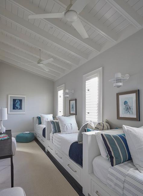 Beach house features a boys' bedroom filled with row of white built-in beds fitted with storage drawers dressed in white and blue striped bedding and pillows lining a single gray wall illuminated by white nautical wall sconces. Beach House Bunk Room, Florida Beach House, Built In Bed, Beach House Interior Design, Bunk Rooms, Home Bunch, Shore House, Dream Beach Houses, Bedroom White