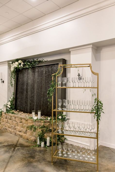 This image features a gold champagne rack for a wedding cocktail hour and entrance. The stand is accented with greenery and next to a water wall with candles, white blooms and greenery. Greenery For Wedding, Candles White, Photography Location, Wedding Champagne, Wedding Entrance, Gold Champagne, Champagne Wedding, Location Photography, Wedding Diy