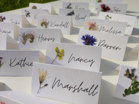 Each card has its own meadow flower, real pressed flower carefully glued on. The cards are already folded and ready to be placed on the table. Perfect for nature inspired wedding, dried flowers wedding, Rustic weddings. White, matte, decorative paper, 250 gsm, is used. You can choose a folded card or a flat card. -The size of a folded card is 9X4.5cm, 3.5X1.7 inches (Full size unfolded 9X9 cm, 3.5X3.5 inches). I can make cards with name and surname. -Flat card size: 9X4.5cm, 3.5X1.7 inches - Tag with golden hole and whatever text you want  size: 10X5 cm, 3.9X1.9 inches.  If you have any special requirements please write to me. Orders over 70 pieces have FREE & EXPRESS SHIPPING. Look here:   https://www.etsy.com/listing/1487518143/pressed-flower-place-cards-with-real?click_key=eca58308b3f2a Wedding Seating Chart Pressed Flowers, Dried Flower Name Card, Pressed Flowers Name Card, Fun Place Cards Wedding, Spring Wedding Name Place Cards, Whimsical Place Setting, Name Cards Table Settings, Name Tag Table Setting, Compostable Wedding Place Settings