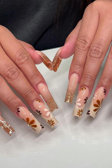 Beautiful Fall mani: Long cutout nails with a nude base, beige French, and fall floral design. Delicate gold glitter specks grace the tips of three nails, while earthy brown, cream, and burnt orange floral accents adorn the others. Simply enchanting! // Photo Credit: Instagram @prettyskulpted Fall Multicolor Nails Acrylic, Beige Acrylic Nails Design, Orange And Brown Nail Designs, Long Square Acrylic Nails Designs Brown, Brown And Cream Nails, Cute Acrylic Nails Designs, Brown And Orange Nails Fall, Super Cute Acrylic Nails, Cutout Nails