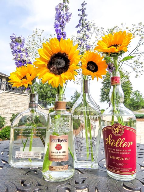 Bourbon Bottle Centerpieces for a "Whiskey & Wildflowers" event theme. Sunflowers, baby's breath, and purple delphiniums. #centerpieces #bourbon #wildflowers #whiskey #eventdesign Bourbon Bottle Vase, Centerpieces With Liquor Bottles, Bourbon Wedding Centerpieces, Bourbon Event Decor, Bourbon Bottles Wedding, Flowers In Bourbon Bottles, Whiskey And Wine Wedding, Whiskey Party Centerpieces, Whiskey Themed Centerpieces