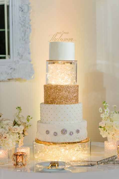 Elegant Bella Cosa Lakeside Wedding | white and gold wedding cake Gold And Cream Wedding Cake, White Wedding Dress With Gold Accents, Wedding Cake Fairy Lights, White Cake With Gold Accents, White And Gold Wedding Cake Elegant, Cakes With Lights, Cake With Fairy Lights, Glitter Cake Ideas, Cake White And Gold