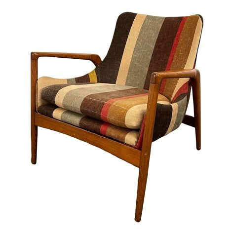 Designed by Ib Kofod Larsen for Christensen & Larsen Design, Denmark c. 1950s. This Larsen chair is absolutely striking in design. It’s sculptural frame is made of solid oak and has beautiful wood grain. The fabric is a large scale stripe featuring colors of blue-grey, beige, red, brown, black, and pops of yellow. Mid Century Modern Chair And Ottoman, 70s Chairs Retro, Brown Chairs Living Room, Mid Century Furniture Living Room, Mcm Ottoman, Mcm Living Room Ideas, Eclectic Minimalism, Denmark Furniture, 1950s Chair