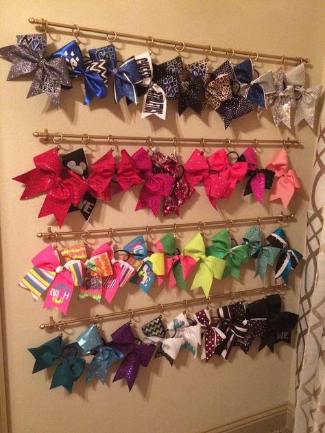 Cheer bow organization--I bought $3 curtain rods and clips with rings at Big Lots (spray painted gold) and attached the bows on the back loop (which doesn't damage the bow). After many years of figuring out how to organize these massive bows, I finally found a solution that works. She simply unclips the bow, wears it, and clips it back up! Cheer Bow Display Ideas, Cheer Bow Storage Ideas, Cheer Bow Holder Diy, Curtain Rods Diy, Cheer Bow Storage, Shelves For Bows, Bow Holder Diy, Bow Organization, Cheer Bow Organizer