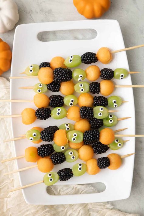 Get ready to spookify your taste buds with our Halloween Fruit Kabobs! These ghoulishly delightful skewers feature juicy cantaloupe balls that are like mini pumpkin orbs, grapes with mischievous googly eyes that seem to watch your every move, and plump, mysterious blackberries that add a dark twist to your fruit adventure. It's a fruity fiesta that's as playful as it is eerie – the perfect way to haunt your taste buds this Halloween! Grab one and take a bite, if you dare! | Halloween F Halloween Fruit Class Party, Halloween Fruit Skewers For Kids, Fruit Kabobs Halloween, Pumpkin With Fruit Skewers, Spooky Fruit Salad, Pumpkin Fruit Kabobs, Fruit Halloween Tray, Halloween Fruit Kabobs For Kids, Halloween Snacks Fruit