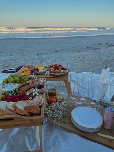 array of 2 charcuterie boards, with a variety of meats, cheeses also seen with flowers, raspberries, blackberries and grapes. aside is champagne flutes with sparkling drinks. all infront of the beach landscape on a sunny spring evening Diy Picnic On The Beach, California Beach Picnic, Beach Picnic Bachelorette Party, Beach Date Picnic, Cute Beach Picnic Ideas, Beach Picnic Bday Party Ideas, Dinner On The Beach Ideas, Bday On The Beach, 21st Birthday At The Beach