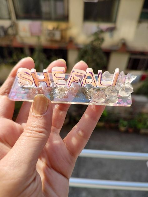 TITLE : Shefali MEDIUM : Resin peach colour, glitter, purple stones and glass crystals in resin SIZE : 4" x 1.5" x 2mm . #MeghnaCreations #shefali #namestand #peachaesthetic #resinpeach #purpleborder #unevenstructure #madeinindiaproducts #transparentbase #glasscrystals #silverglitter #purplestone #smallfont #names #make #purpose #artistically #closeshots #nameeffect #eachuniqueintheirownway #birdschirping Crystals In Resin, Resin Name Plate, Wrapping Gift Baskets, Handmade Rakhi Designs, Creative Wedding Gifts, Handmade Rakhi, Rakhi Design, Peach Colour, Peach Aesthetic