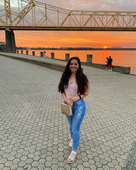 Pose by a sunset reflecting off water. Outfit ideas: pink tank too with light wash denim jeans. Open toes sandals with a gold purse. Hair down with sparkly hoop earrings #travel #roadtrip #Louisville #kentucky #sunset #bridge #water #ohio #river Sparkly Sandals Outfit, Water Outfit Ideas, Kentucky Sunset, Water Outfit, Travel Poses, Sunset Bridge, Outfit Ideas Pink, Travel Pose, Light Wash Denim Jeans