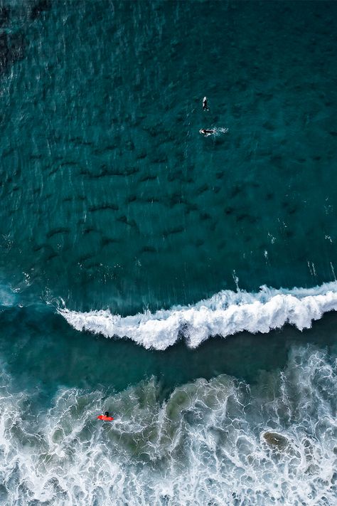 Waves and surfers in the blue water of the sea seen from above.