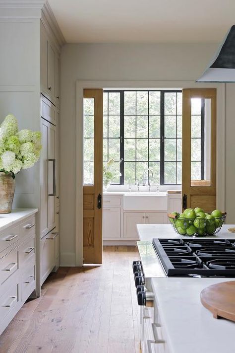 An oak pocket door opens to reveal a farmhouse kitchen sink fitted over white shaker cabinets and paired with a polished nickel deck mount faucet mounted to a honed marble countertop in front of black framed windows. White Kitchen Inspiration, Best Kitchen Design, Beautiful Kitchen Designs, Ideas Hogar, White Kitchen Design, Pocket Door, Kitchen Farmhouse, Futurism, Pocket Doors