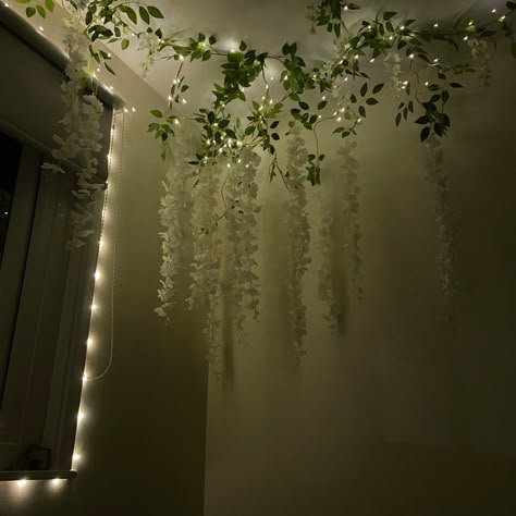 Celling decorated with white wisteria flowers and fairy lights. Night time. Ivy Fairy Lights Living Room, Vines And Fairy Lights Hanging From Ceiling, White Wisteria Bedroom Decor, Bedroom Decor Ideas Fairy Lights, Bedroom Ceiling Ideas Diy Fairy Lights, Wisteria Corner Bedroom, Wisteria On Ceiling Bedroom, Hanging Flower Vines, Vine Lights On Ceiling