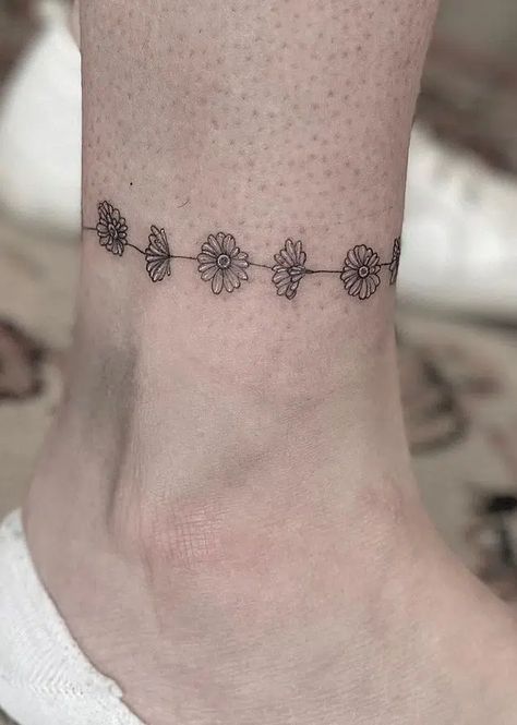 The Meaning of Daisy Tattoos: A Guide to Interpretations Daisy Chain Tattoo Ankle, Daisy Tattoo Ideas, Braclet Tattoo, Daisy Tattoo Meaning, Daisy Chain Tattoo, Anklet Tattoos For Women, Small Daisy Tattoo, Daisy Tattoos, Wrap Around Wrist Tattoos